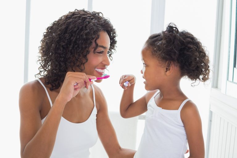Smiling mother and daughter brushing their teeth together in a bright bathroom
