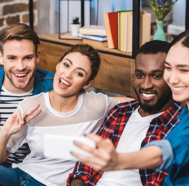 Diverse group of young adults smiling and taking a selfie together, showing bright and healthy teeth