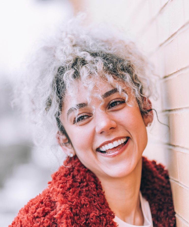 Smiling woman with bright teeth leaning against wall after dental crown treatment