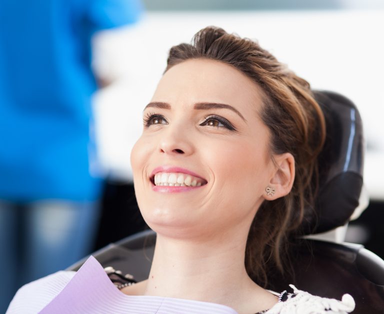 Happy woman sitting in a dental chair, smiling after veneer treatment