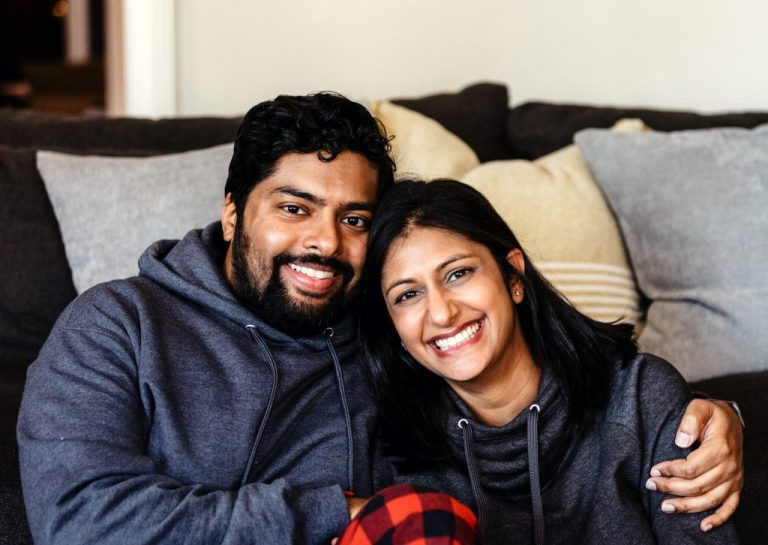 Happy couple sitting on a couch, smiling confidently after receiving dental bonding treatments