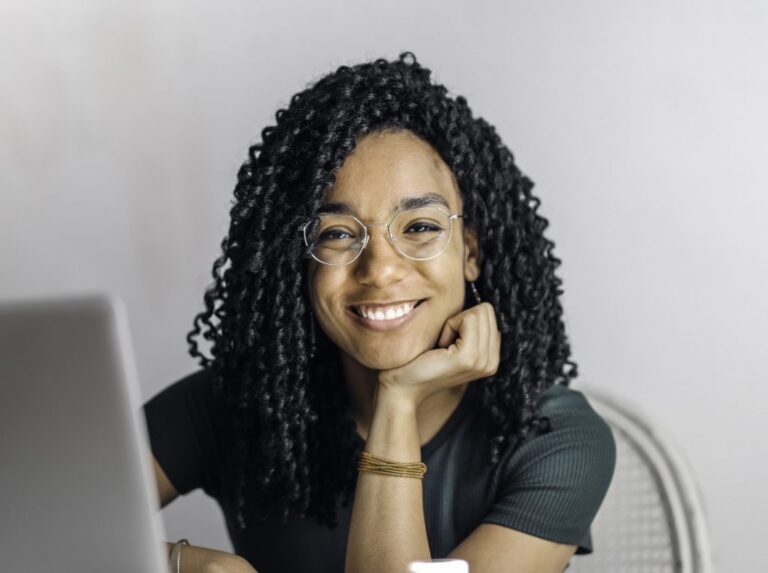 Confident young woman smiling at her desk, showing healthy teeth after dental implants