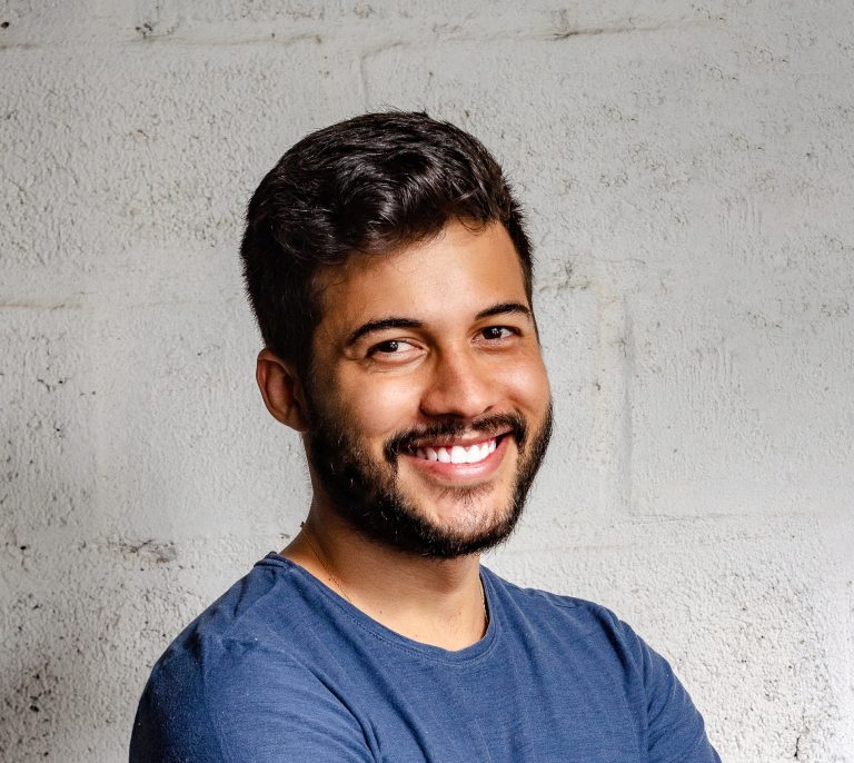 Young man with a beard smiling confidently in front of a textured white wall