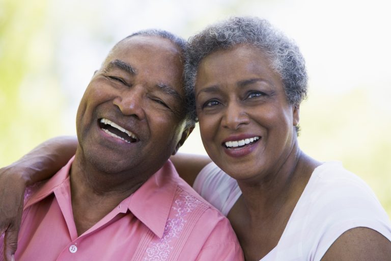 Smiling elderly couple enjoying time outdoors, showing bright smiles with dentures