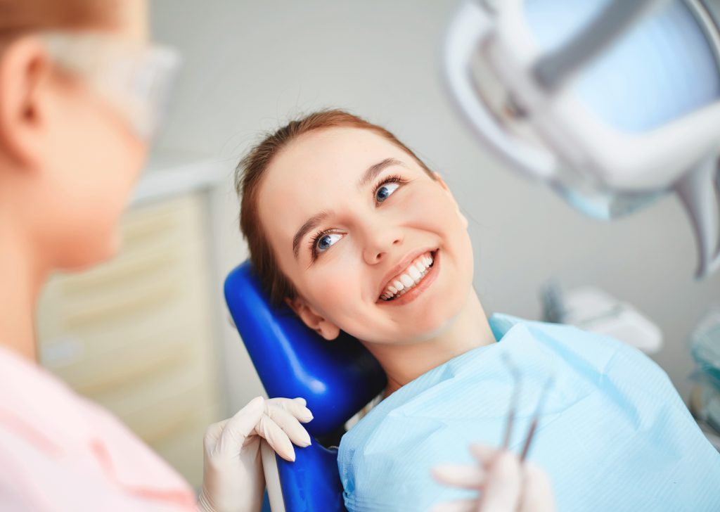Young woman smiling in a dental chair, interacting with dentist after receiving a tooth filling