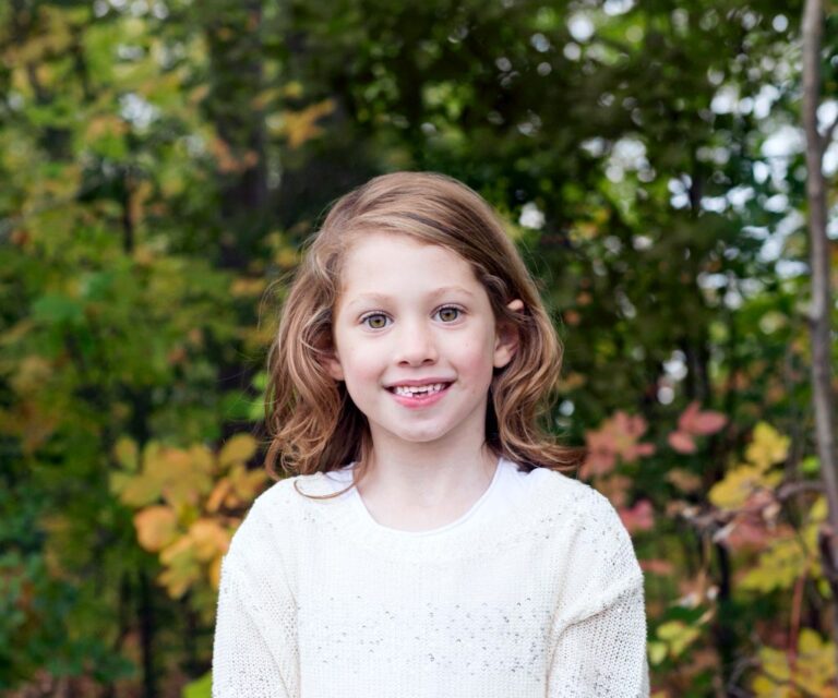 Portrait of a smiling young girl with healthy teeth standing in a natural outdoor setting
