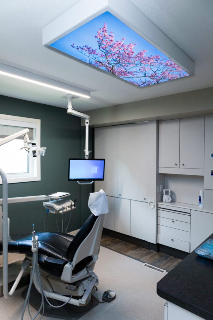 Spacious dental treatment room at Orchard Family Dental in Leduc featuring advanced equipment and calming ceiling artwork