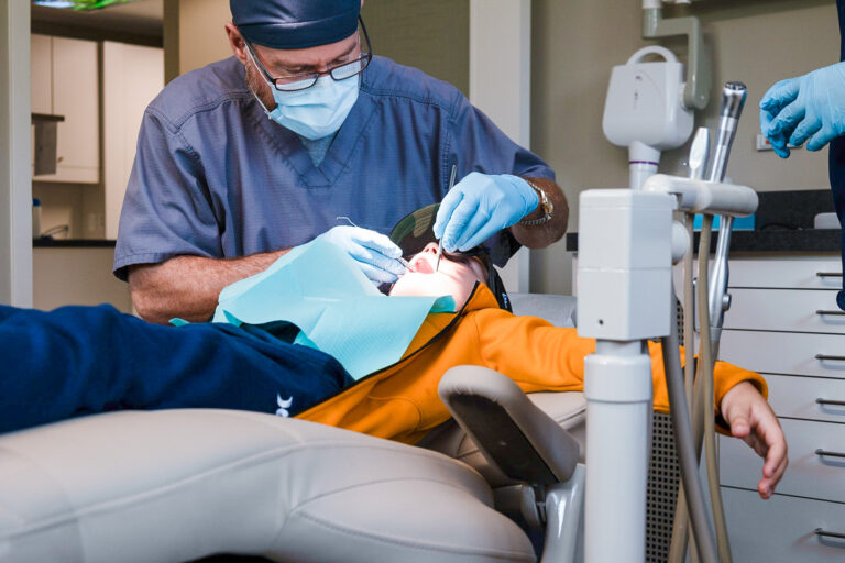 Dentist performing a procedure on a child patient in a treatment room at Orchard Family Dental in Leduc