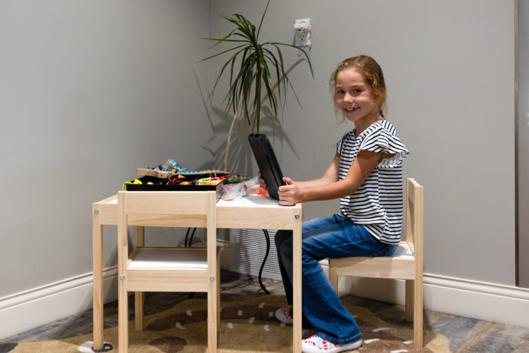 Young girl sitting at a small table using a tablet in a dental office children’s play area