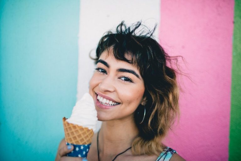 Young woman smiling brightly while holding an ice cream cone, showing off straight white teeth after cosmetic dental treatment