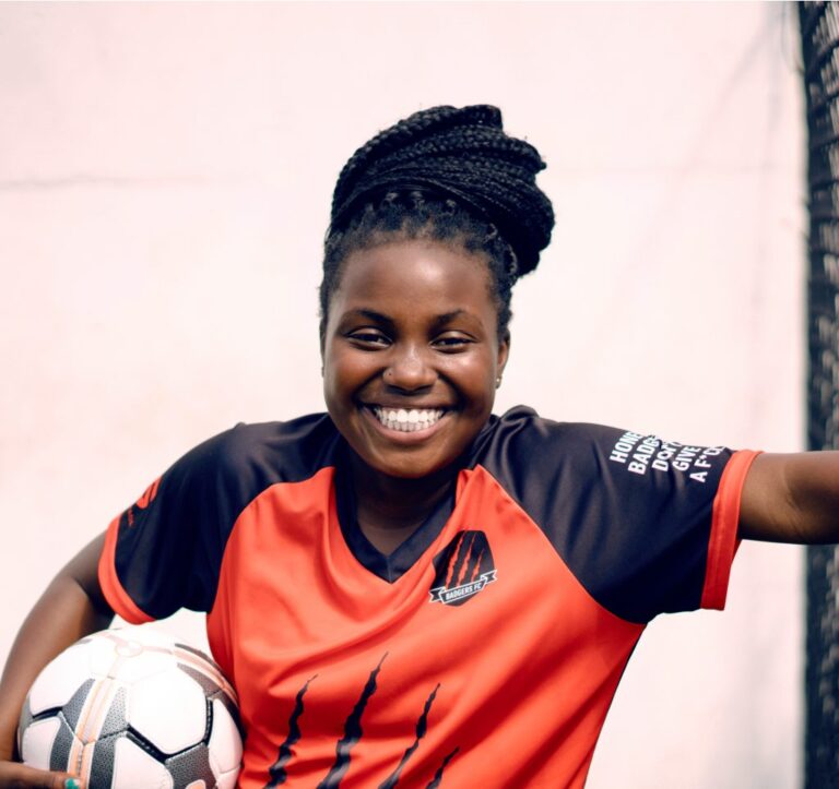 Young female soccer player smiling confidently while wearing a custom sports mouthguard, holding a soccer ball in team uniform