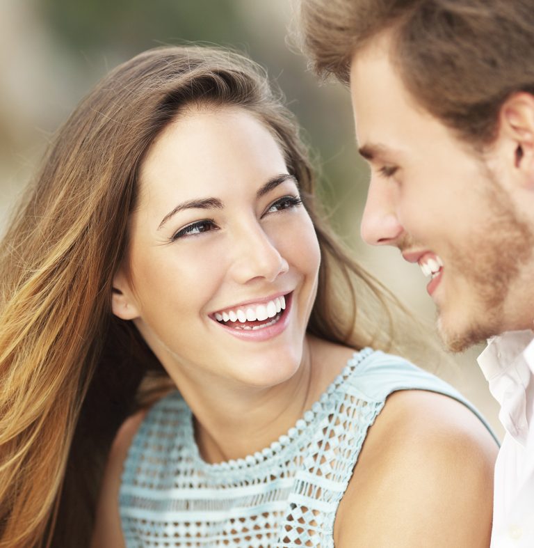 Happy couple smiling at each other, showing bright white teeth after dental whitening