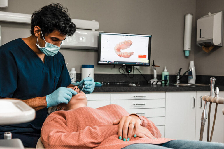 Dentist examining a patient while digital dental impressions are displayed on-screen at Orchard Family Dental in Leduc