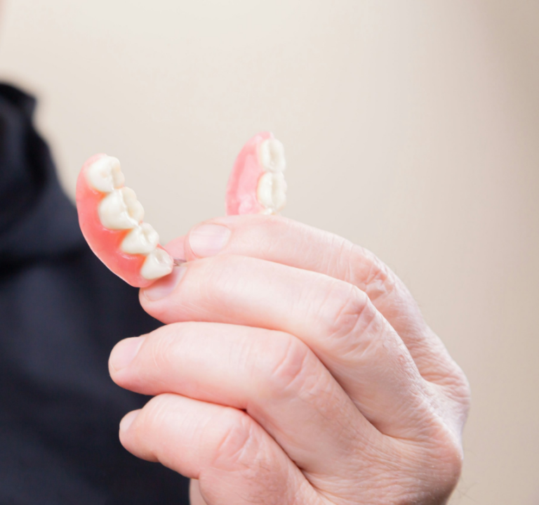 Close-up of a hand holding removable partial dentures with artificial teeth